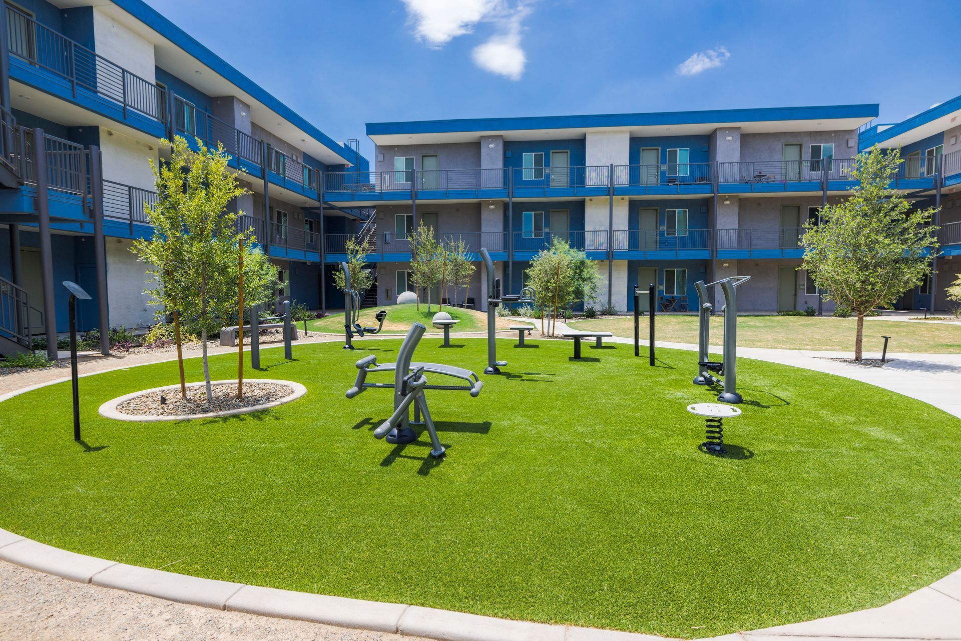 Courtyard with outdoor fitness equipment; blue and white apartment complex in the background.