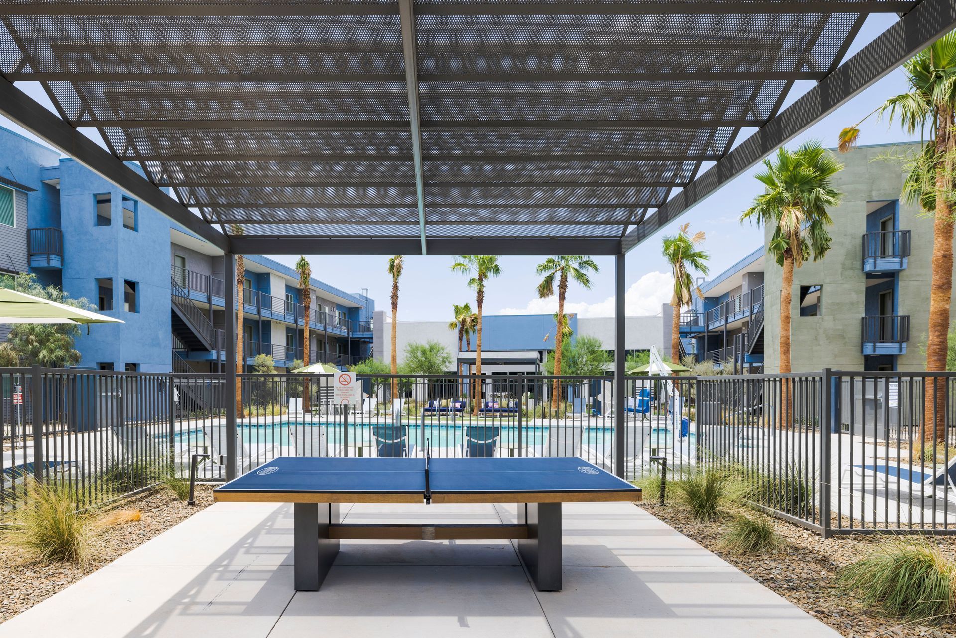Ping pong table under a pergola, overlooking a pool and apartment buildings.