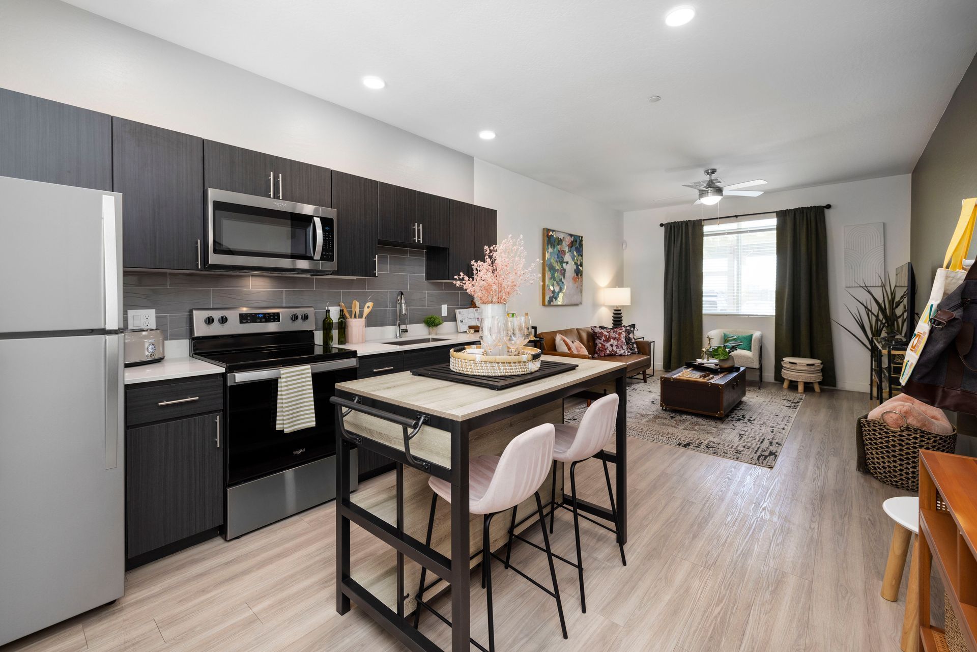 Modern open-plan apartment with kitchen island and living area. Gray and wood tones dominate the decor.