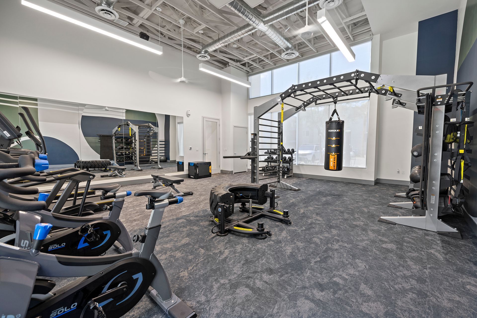 Bright gym with spin bikes, weight machines, a punching bag, and large windows.