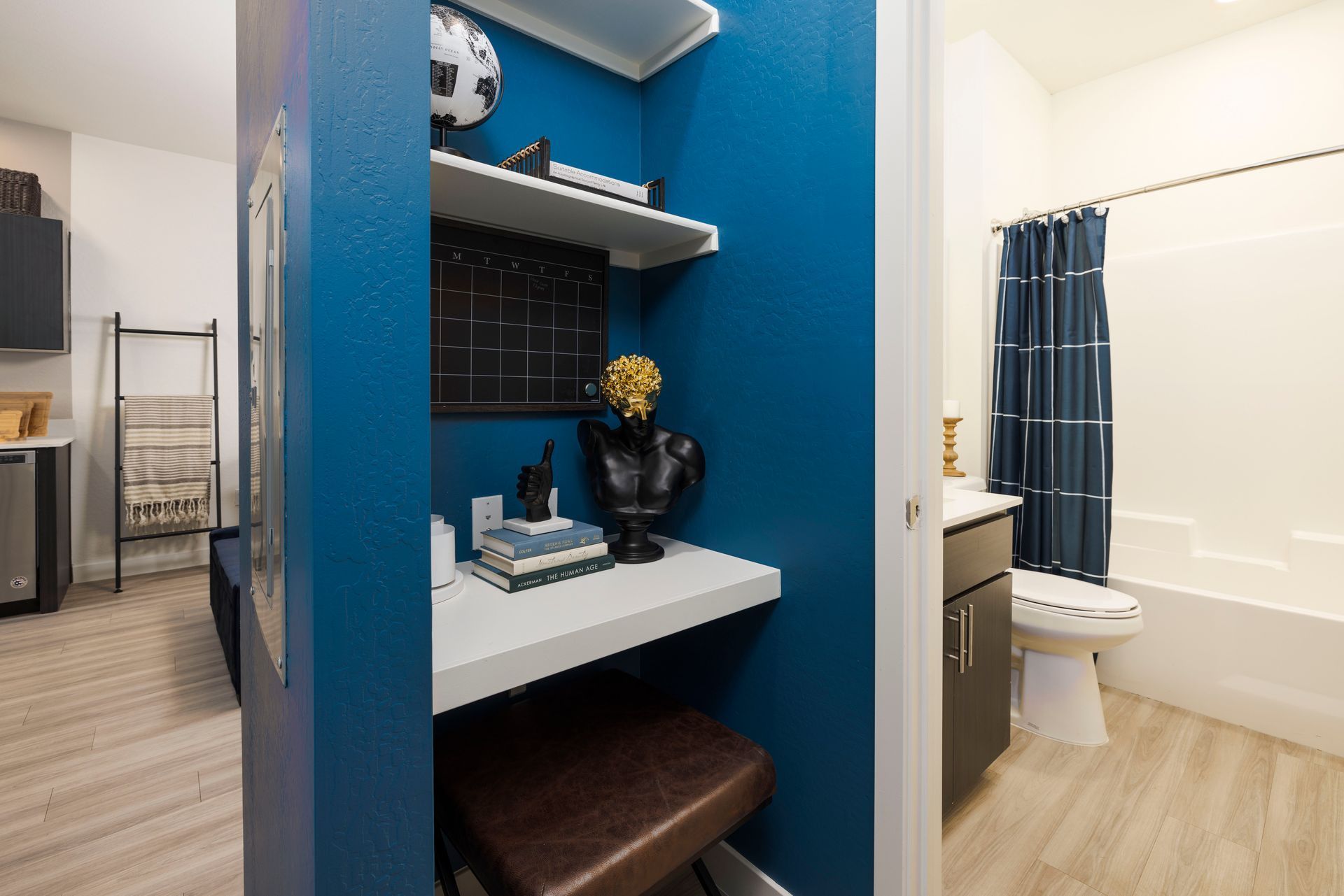 Blue study nook with desk, shelf, and stool next to a bathroom with a blue shower curtain.