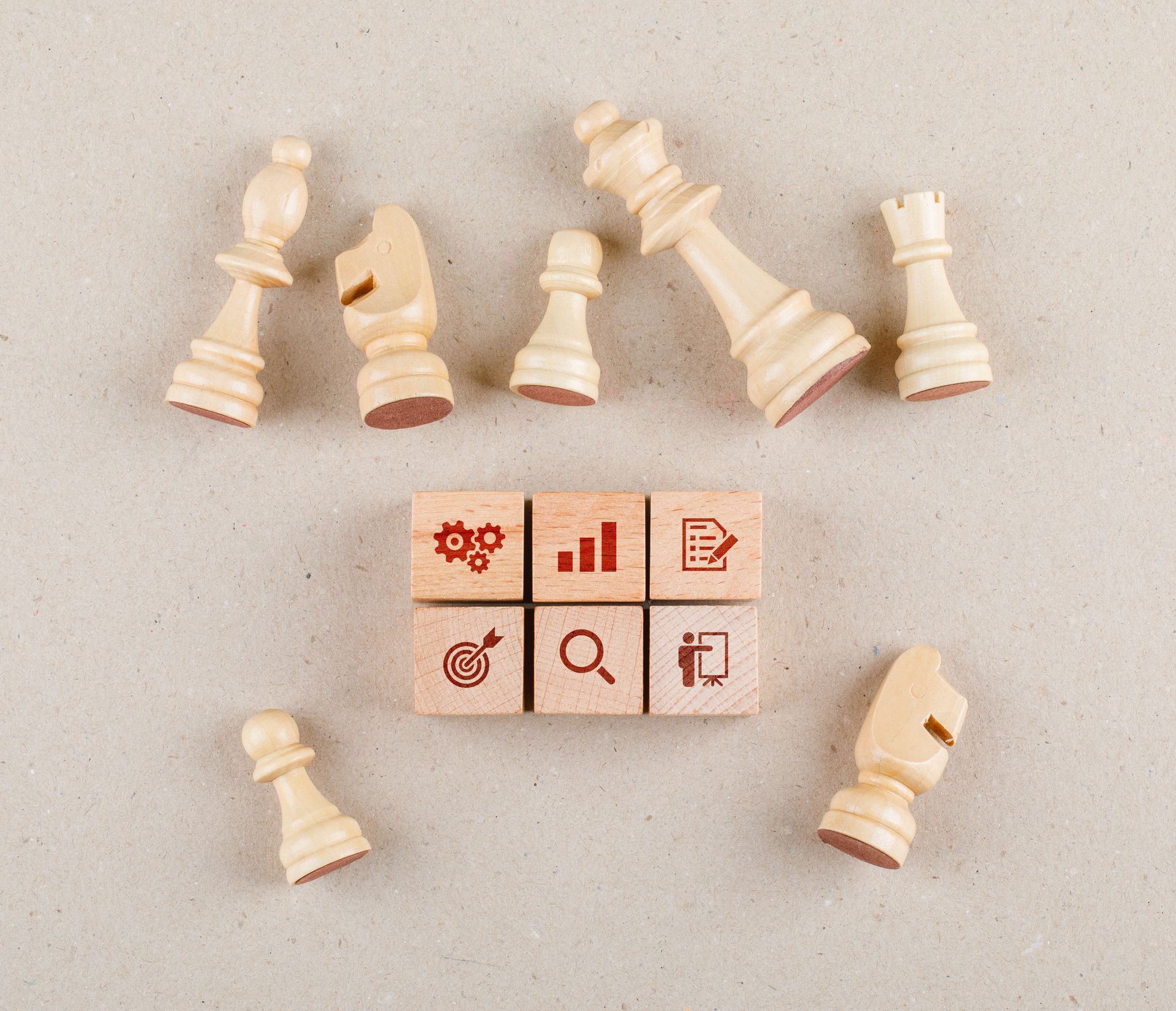 Wooden chess pieces arranged around six small wooden cubes with red business icons on a neutral textured background.