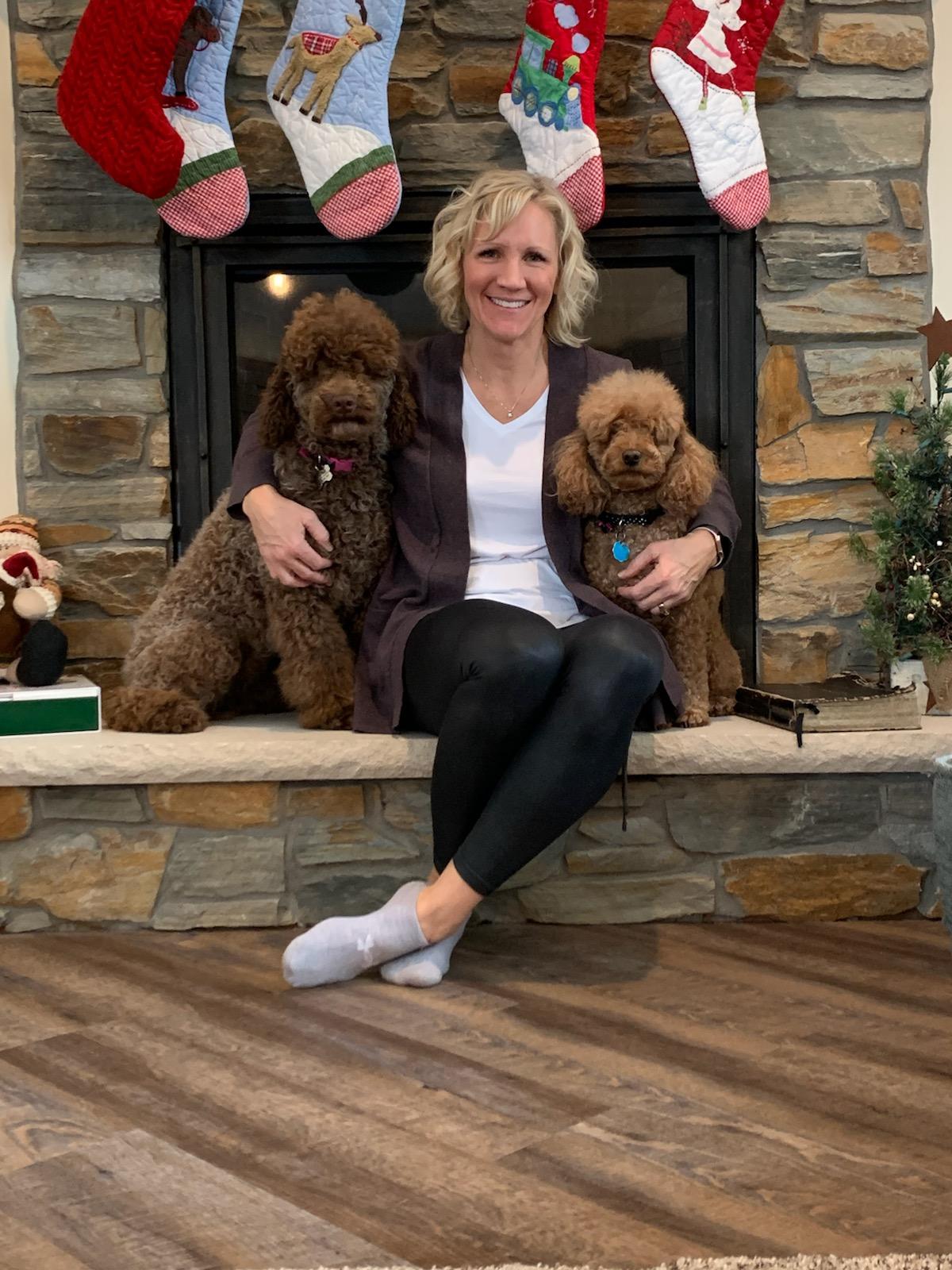 A woman is sitting on a fireplace ledge with two dogs.