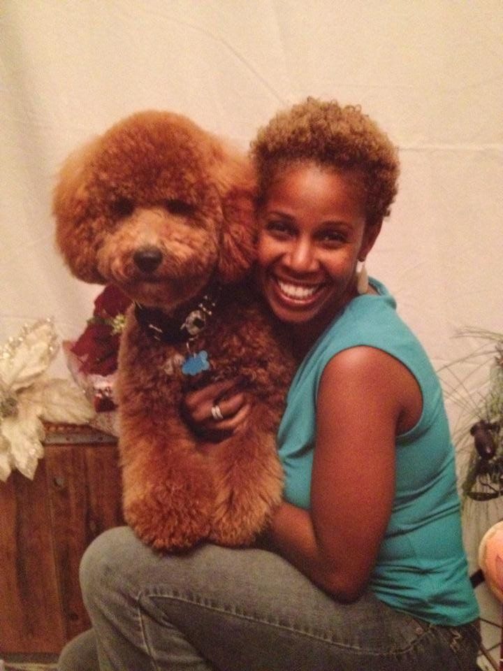 A woman in a blue shirt is holding a brown poodle