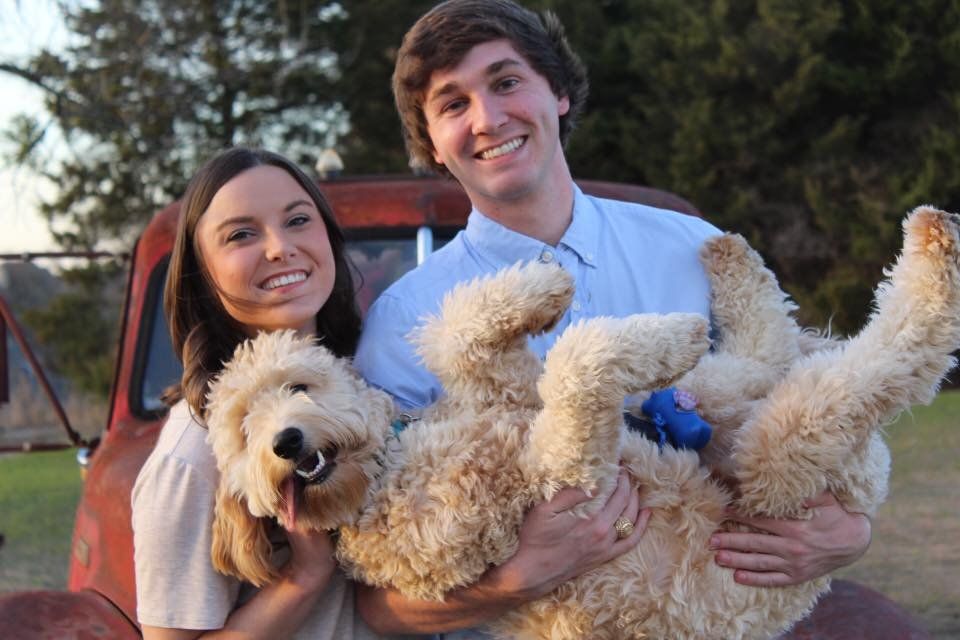A man and a woman are holding a dog in front of a red truck.