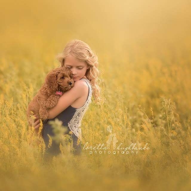 A young girl is holding a small brown dog in a field.