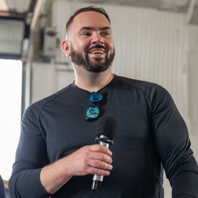 A man with a beard is holding a microphone and smiling.