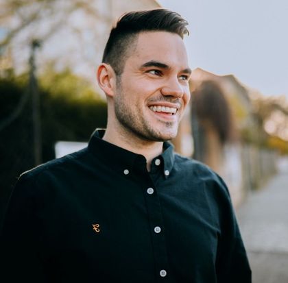 A man in a black shirt is smiling and looking to the side.