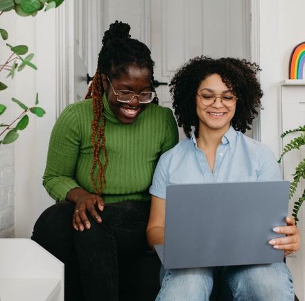 Two women are sitting next to each other looking at a laptop.