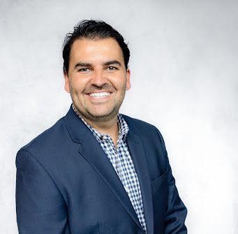 A man in a suit and plaid shirt is smiling for the camera.