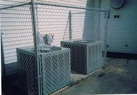 Two air conditioners are behind a chain link fence