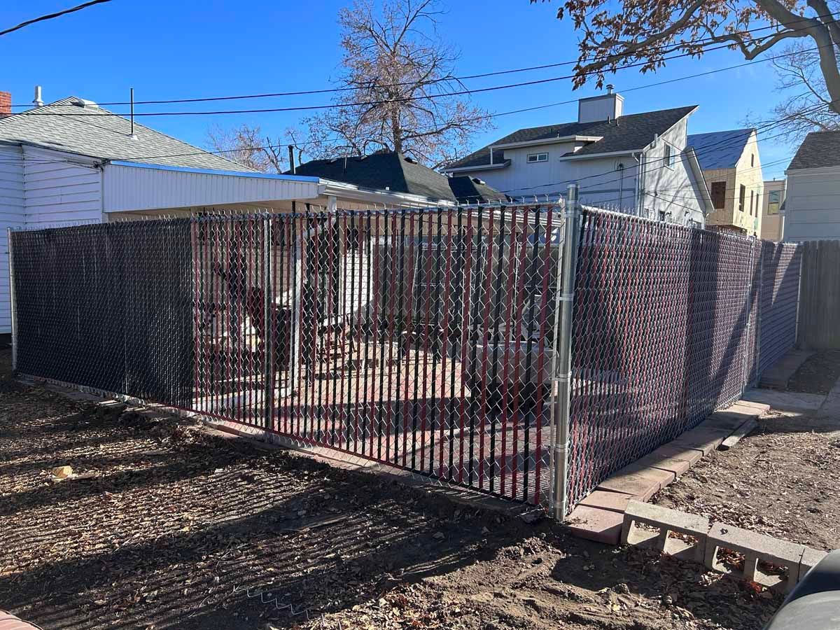 A chain link fence is surrounding a yard in front of a house.