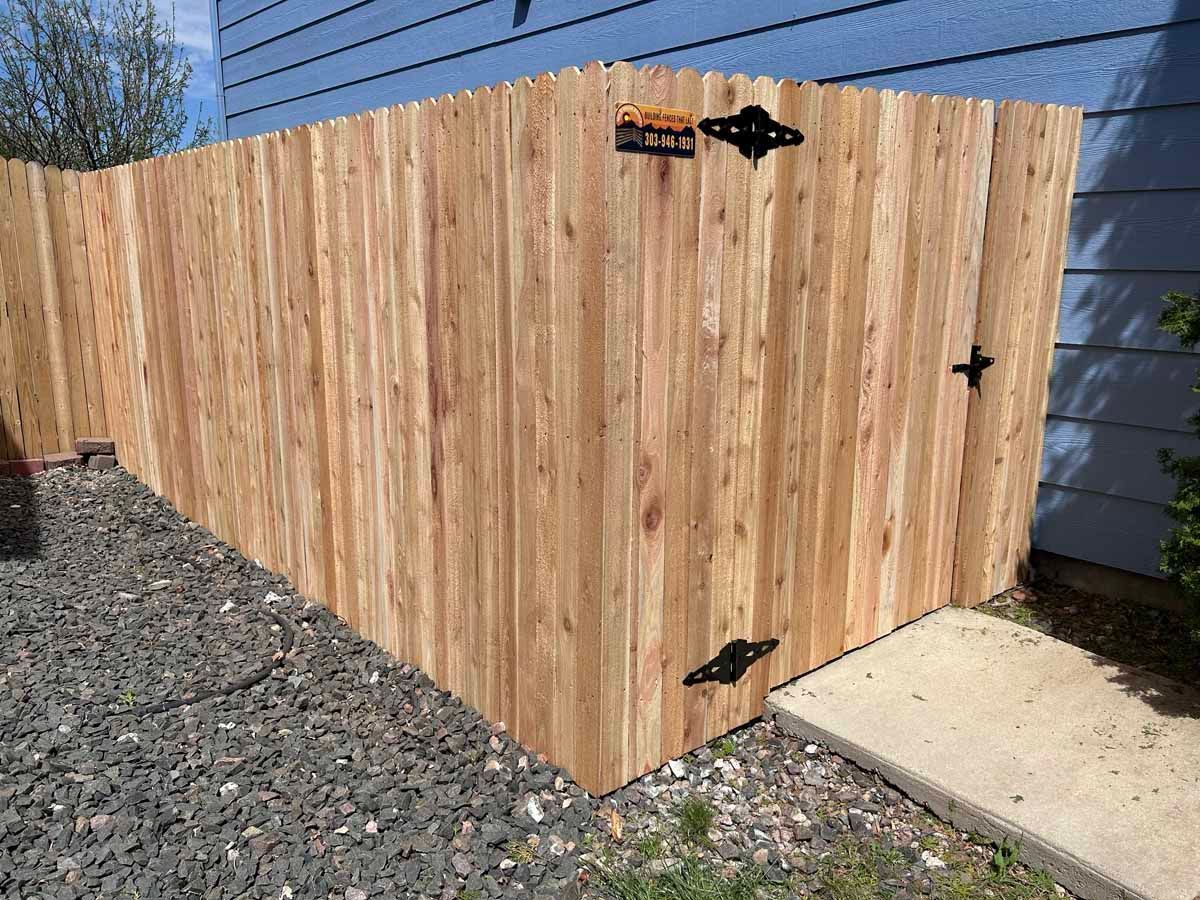 A wooden fence is sitting next to a sidewalk in front of a house.