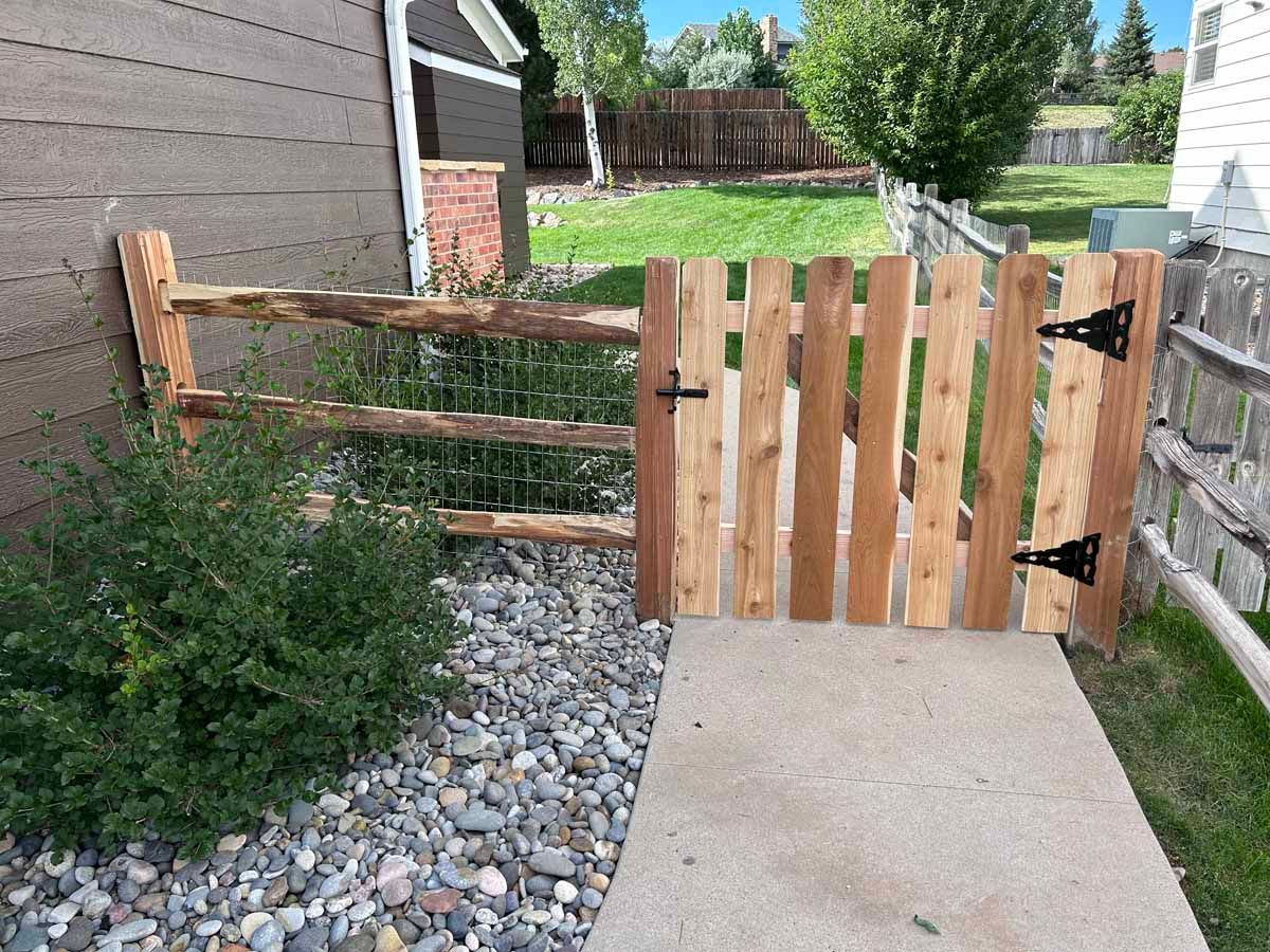 A wooden gate is sitting on a sidewalk next to a house.