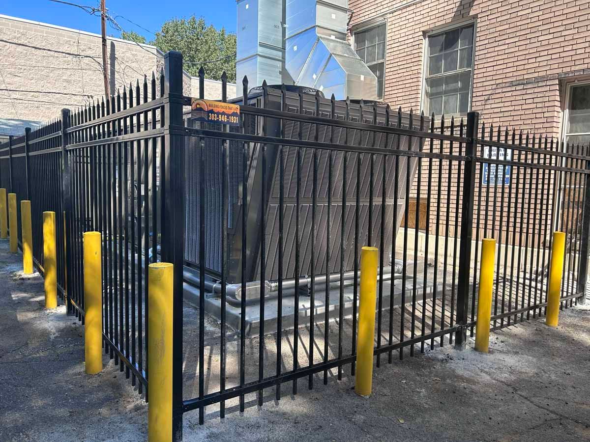 A black metal fence with yellow poles is surrounding a building.