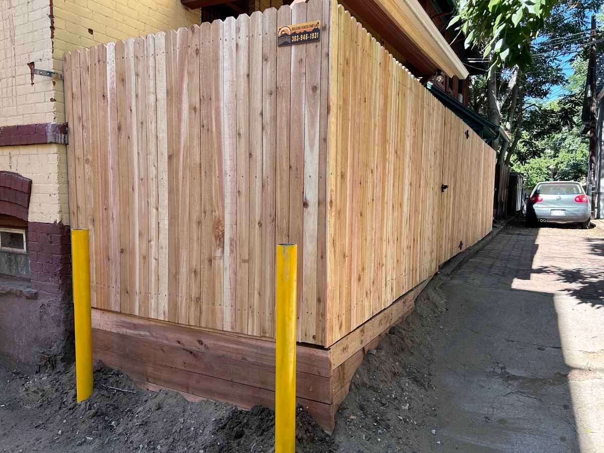A wooden fence is sitting on the side of a road next to a building.