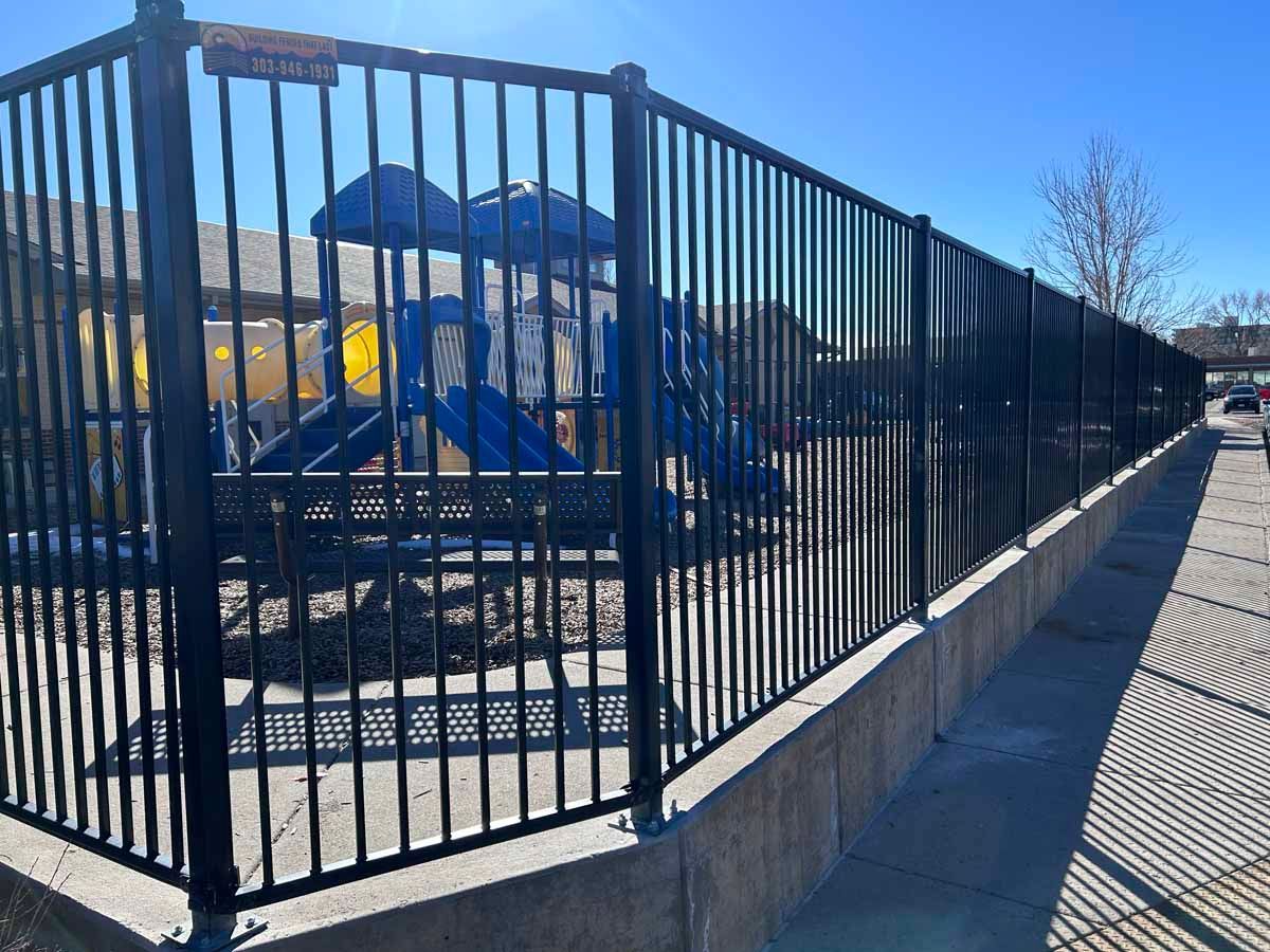 A black metal fence surrounds a playground in a park.