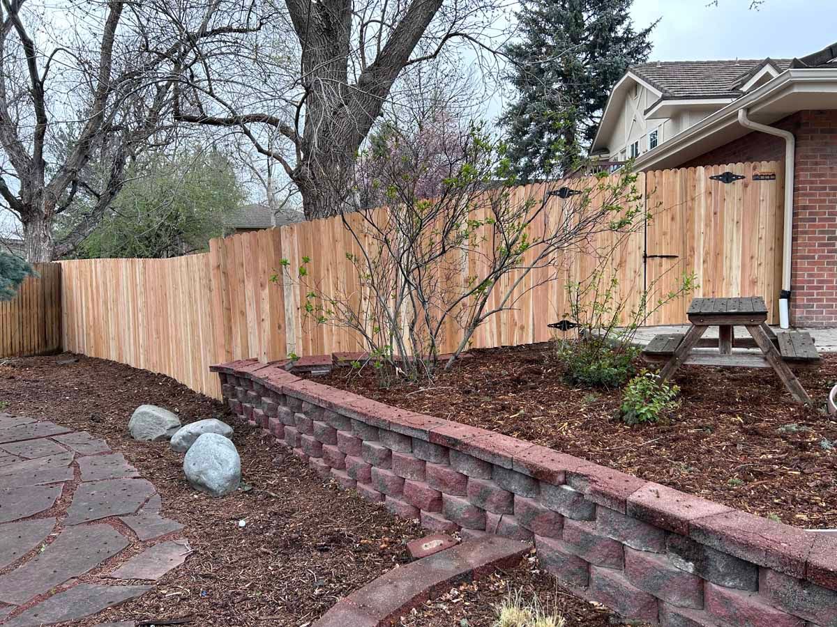 A wooden fence surrounds a brick wall in front of a house.