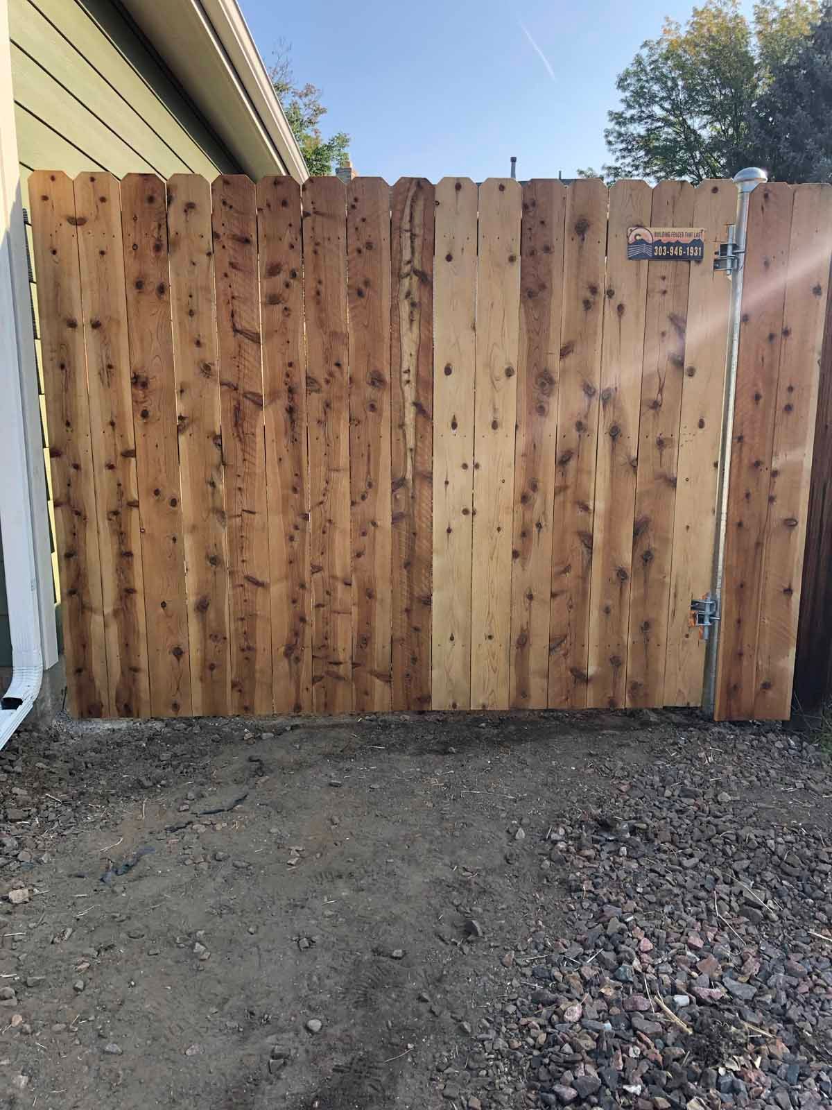 A wooden fence is sitting in the dirt in front of a house.