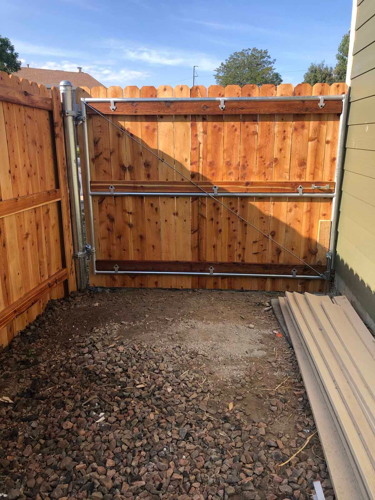A wooden fence with a metal gate in the backyard of a house.