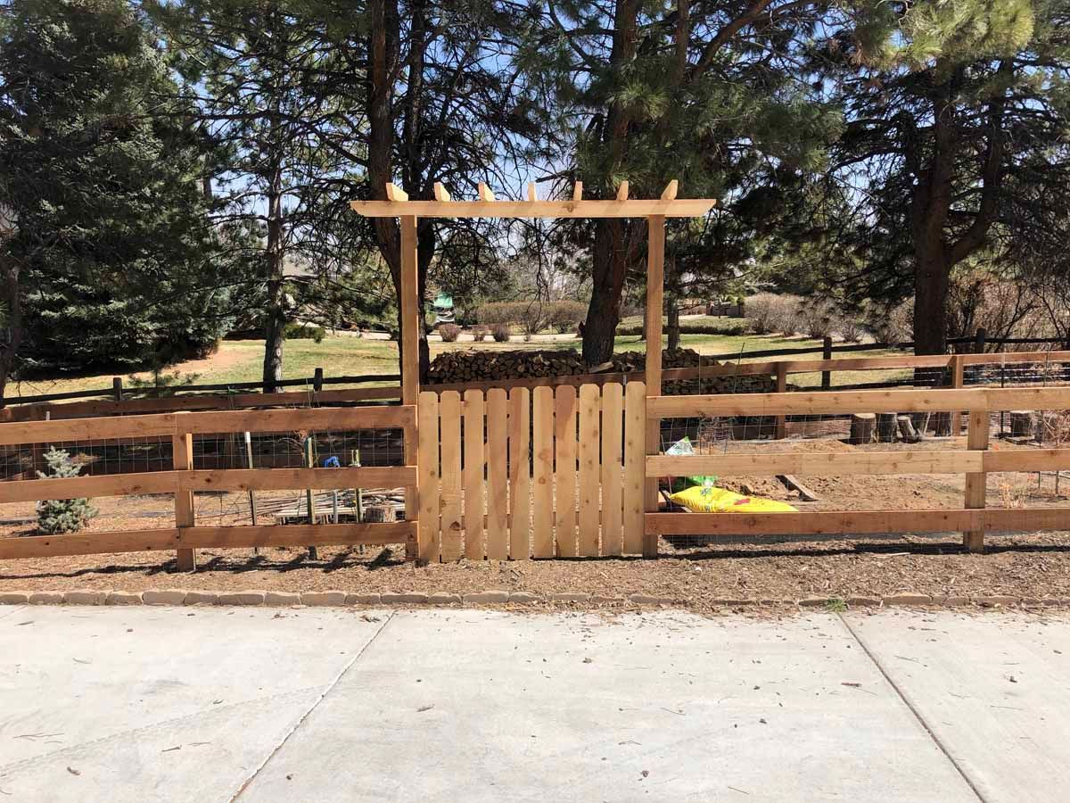 A wooden fence with a gate and a pergola in the middle of a park.