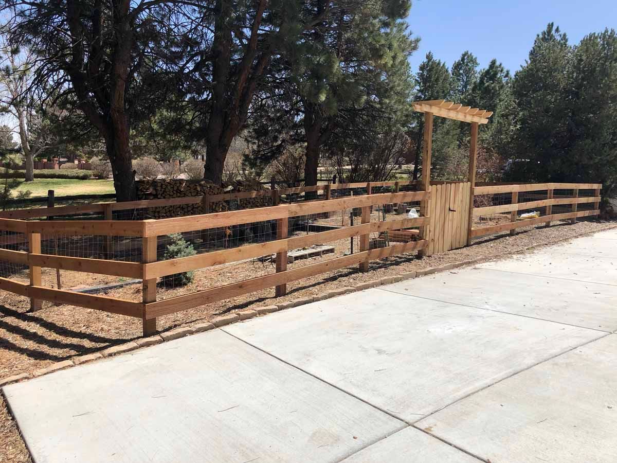 A wooden fence surrounds a concrete driveway with trees in the background.