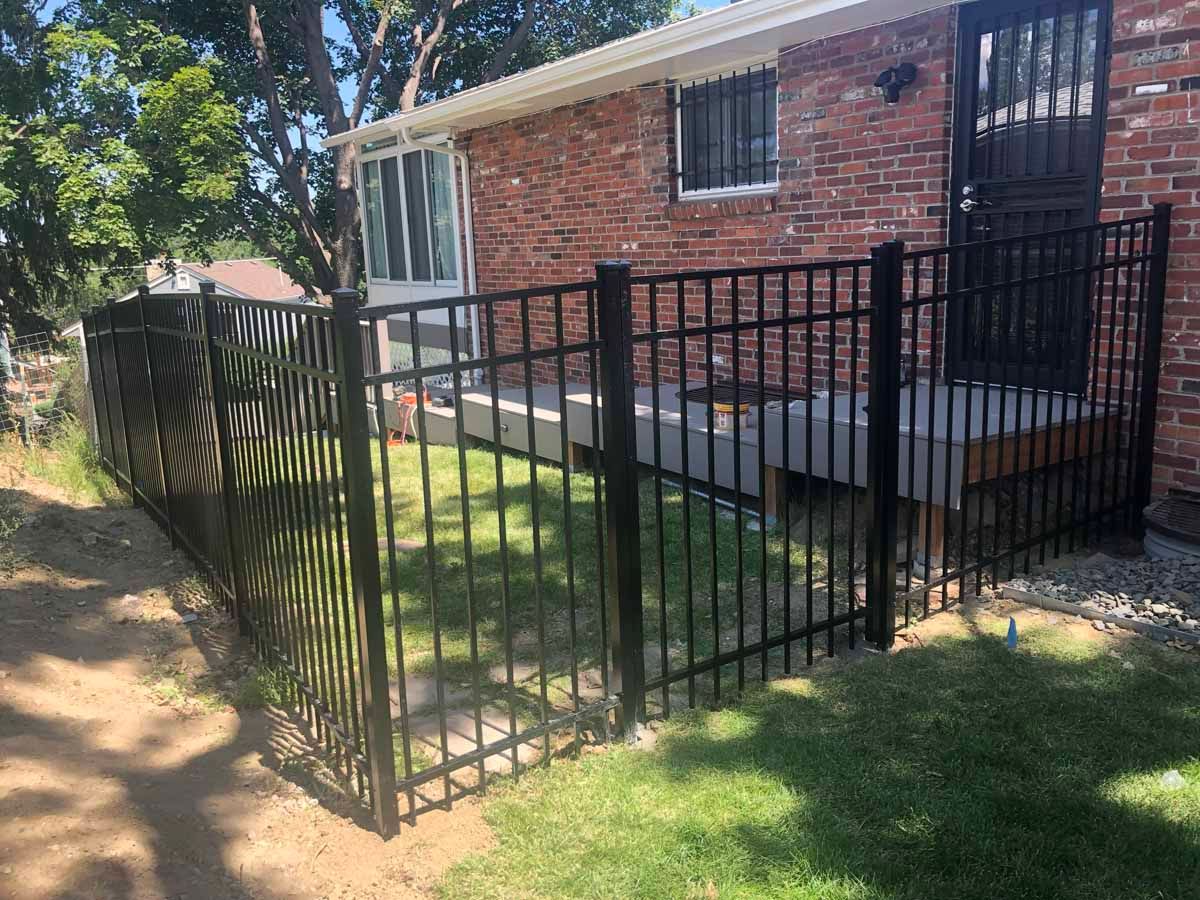 A black fence is in front of a brick house.