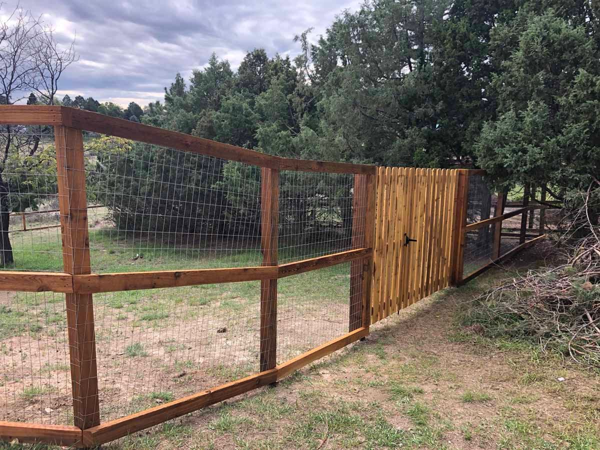 A wooden fence with a gate in the middle of a grassy field.