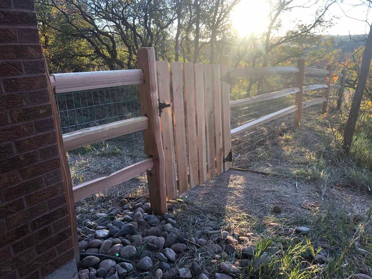 A wooden fence with a gate is next to a brick building.