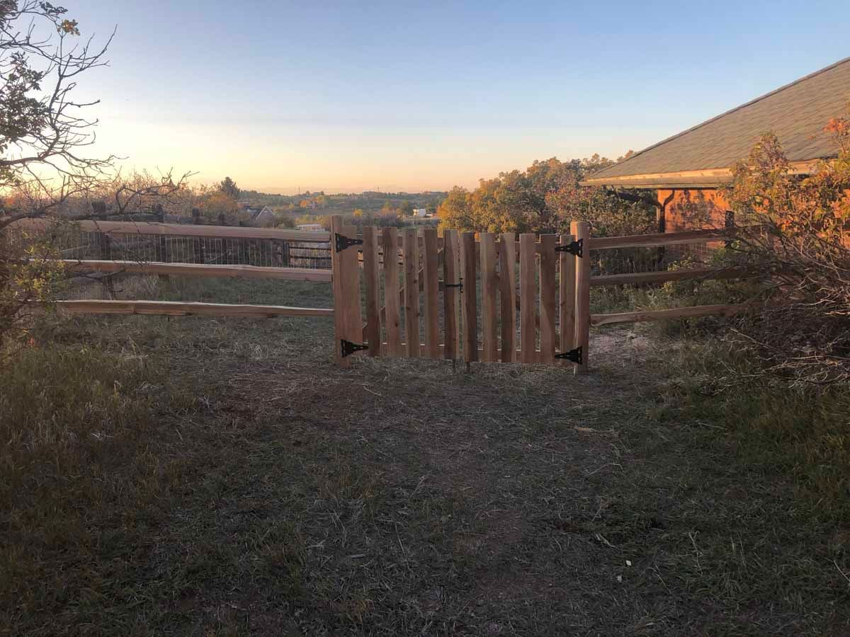 A wooden fence is sitting in the middle of a grassy field next to a house.