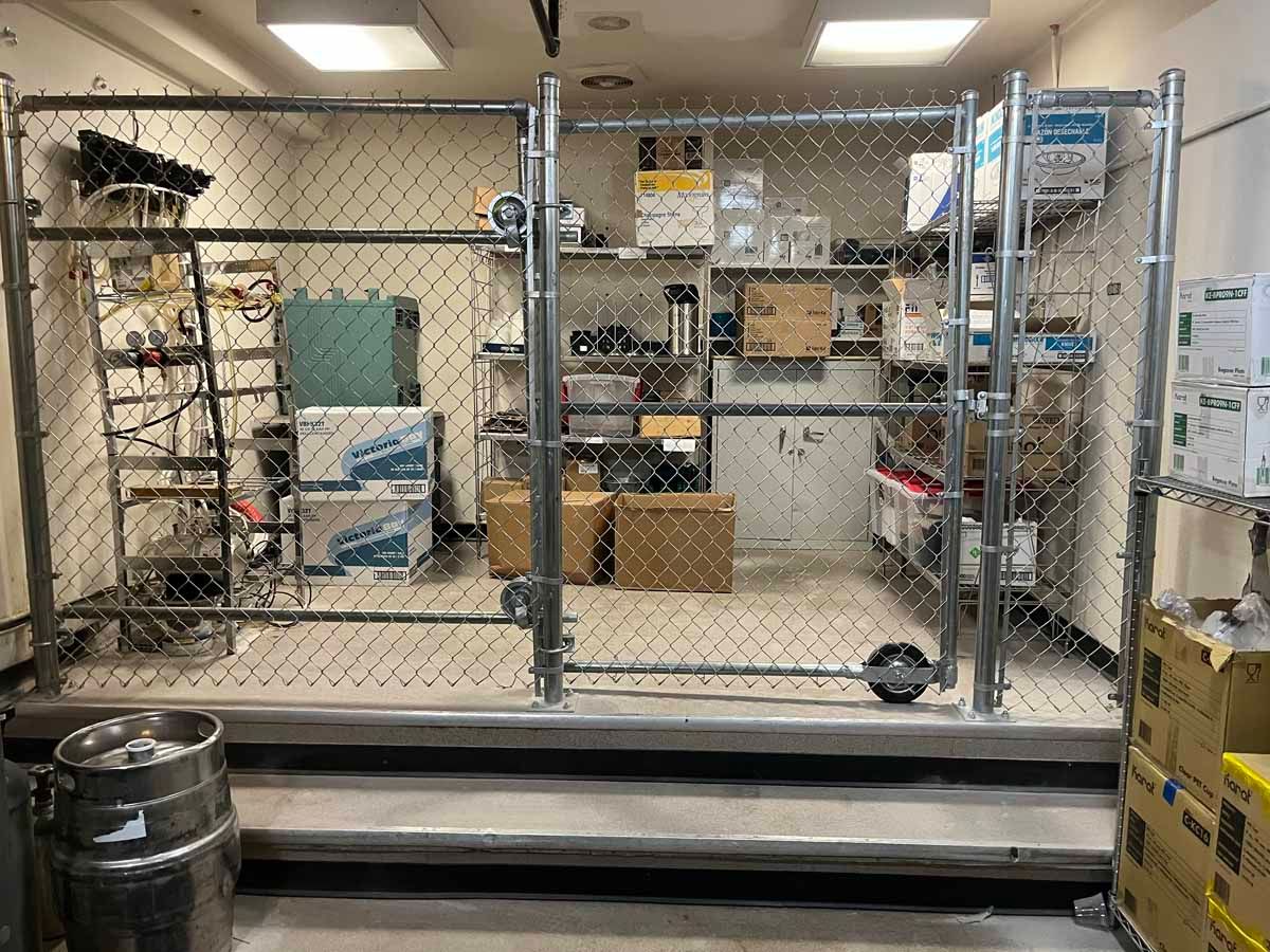 A chain link fence is surrounding a room with shelves and boxes.