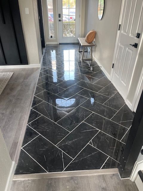 Herringbone pattern black tile flooring in a foyer with white doors, neutral walls, and a small bench.