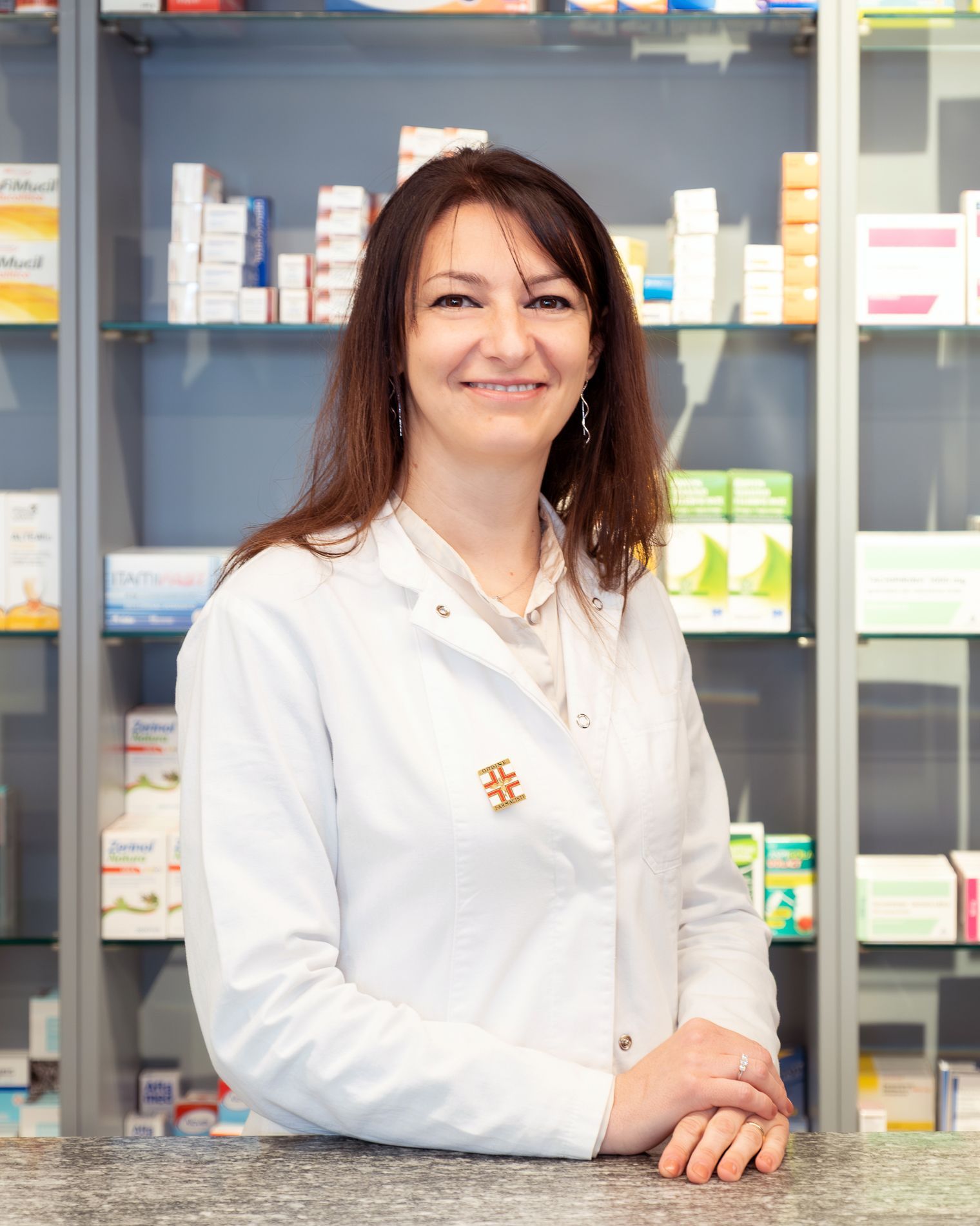 Una donna con un camice bianco è seduta al bancone di una farmacia.