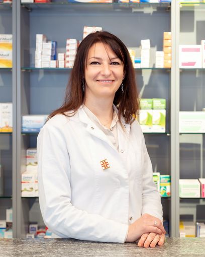 Una donna con un camice bianco è seduta al bancone di una farmacia.
