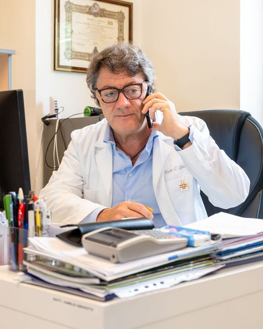 Un uomo in camice è seduto a una scrivania e parla al cellulare.