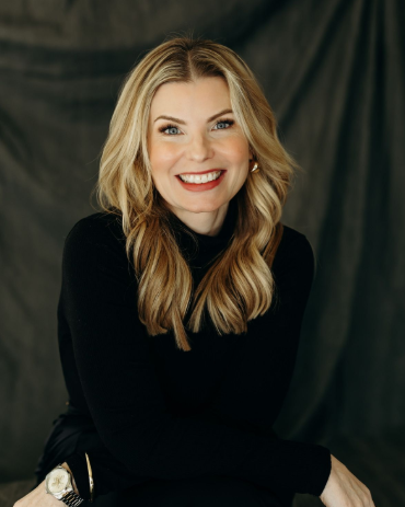 Smiling woman in a black top seated against a dark backdrop.