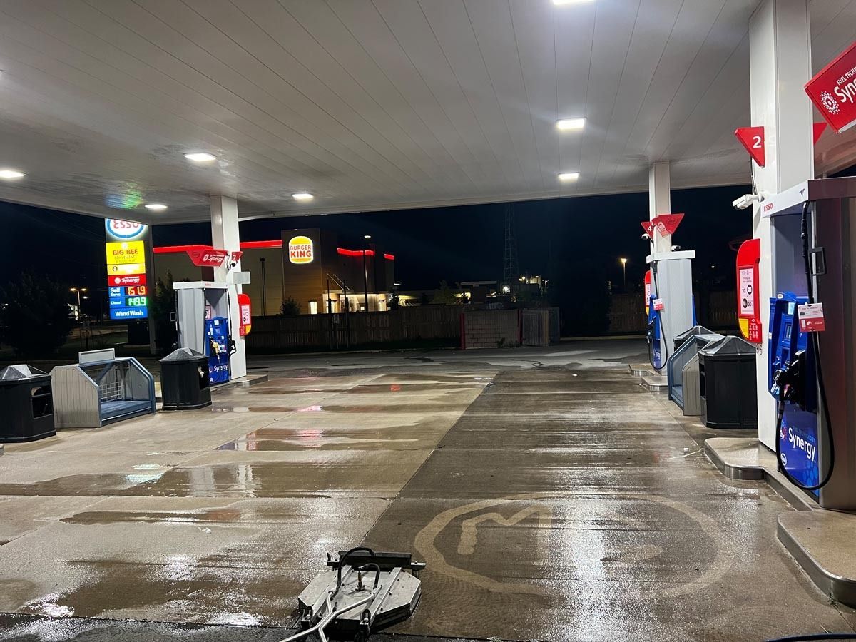 An empty gas station at night with a motorcycle parked in front of it.
