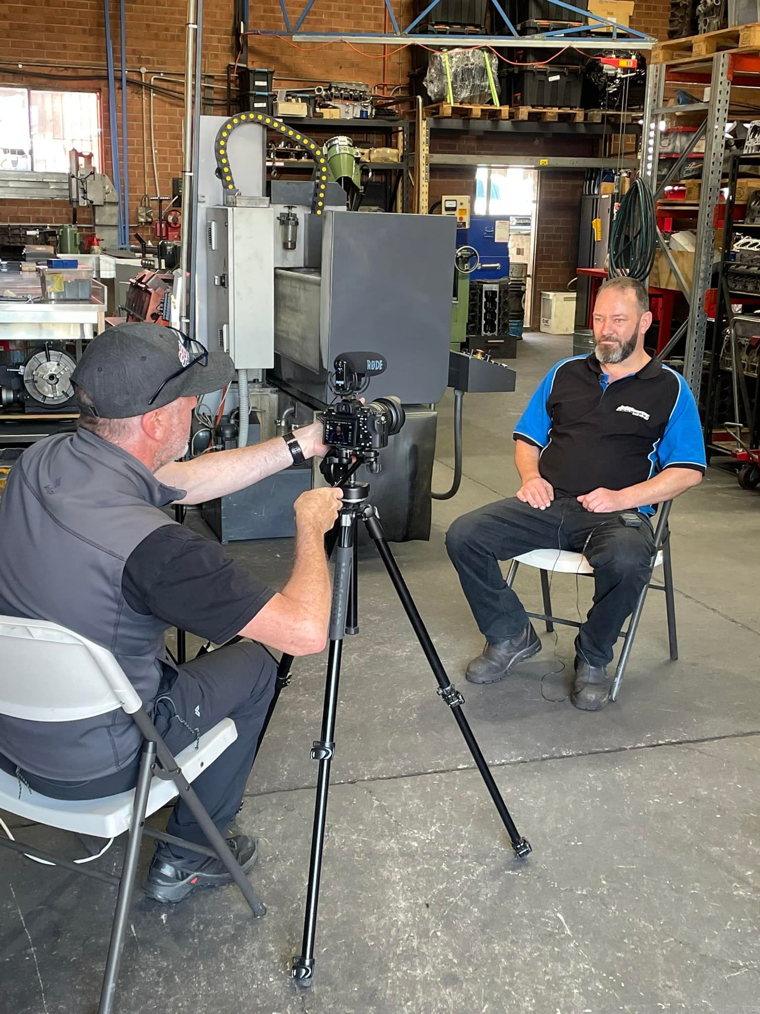 A man is sitting in a chair in front of a camera while another man takes a picture of him.