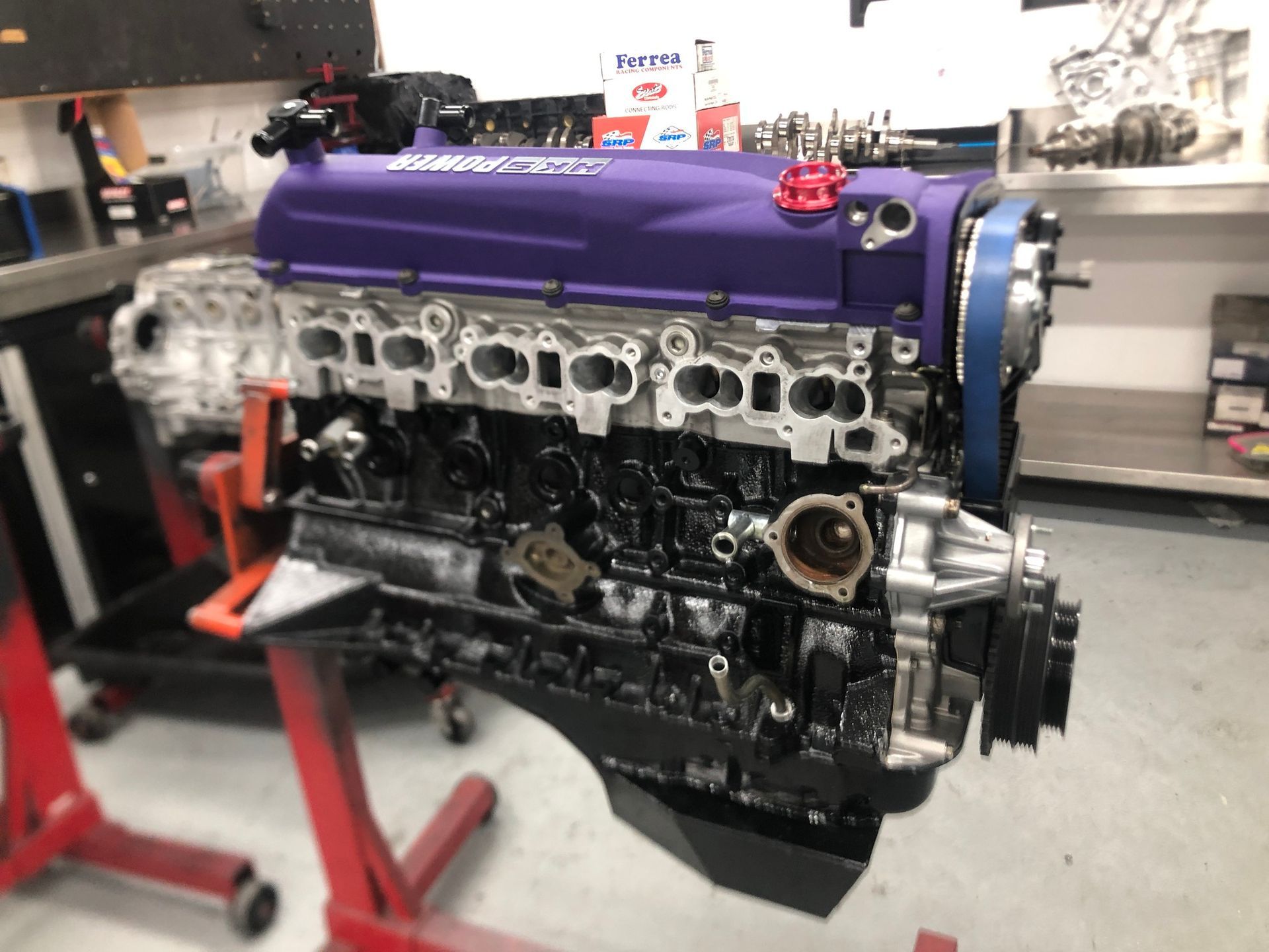 A purple engine is sitting on a red stand in a garage.
