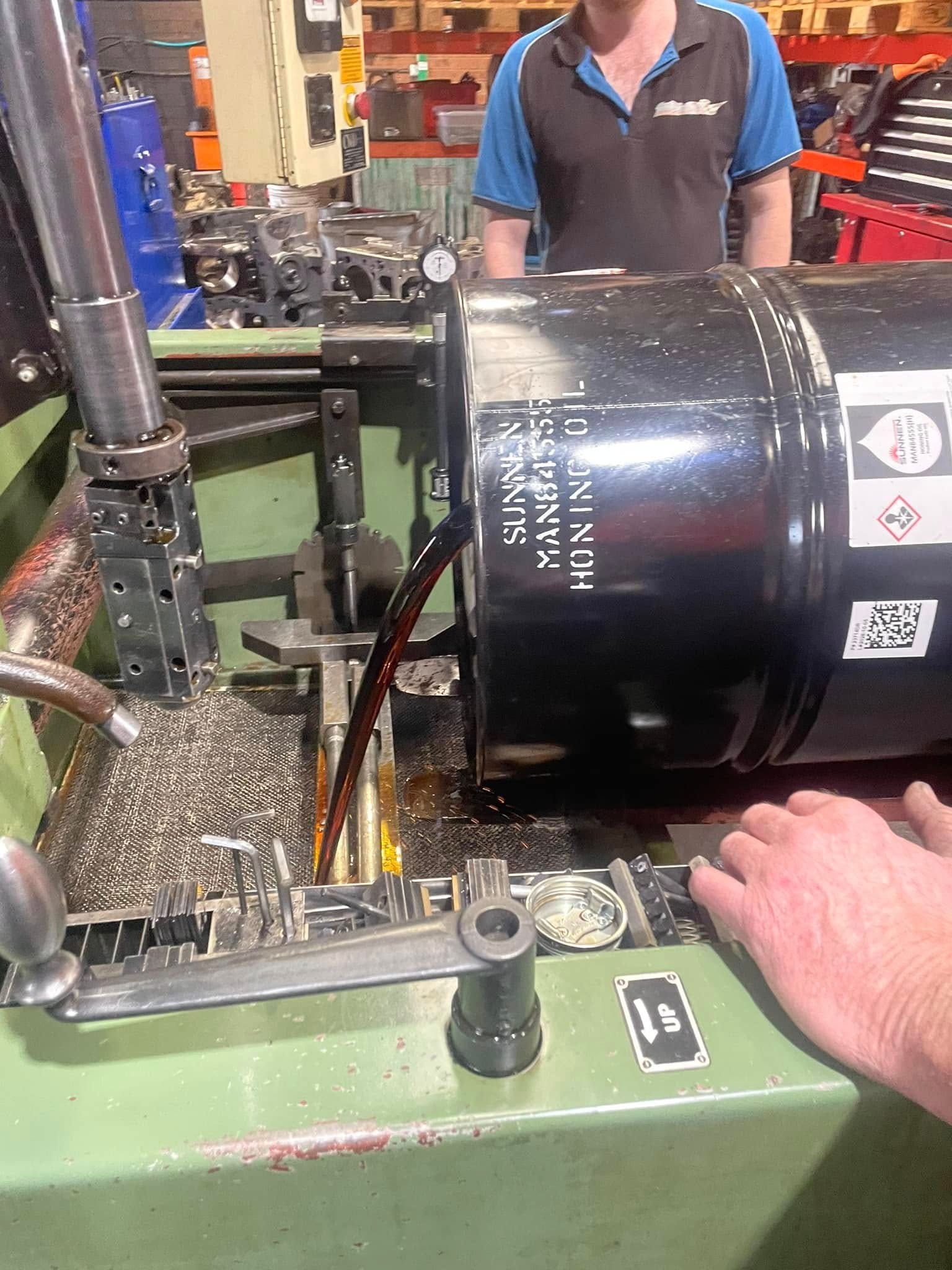 A man is pouring oil into a barrel on a machine.