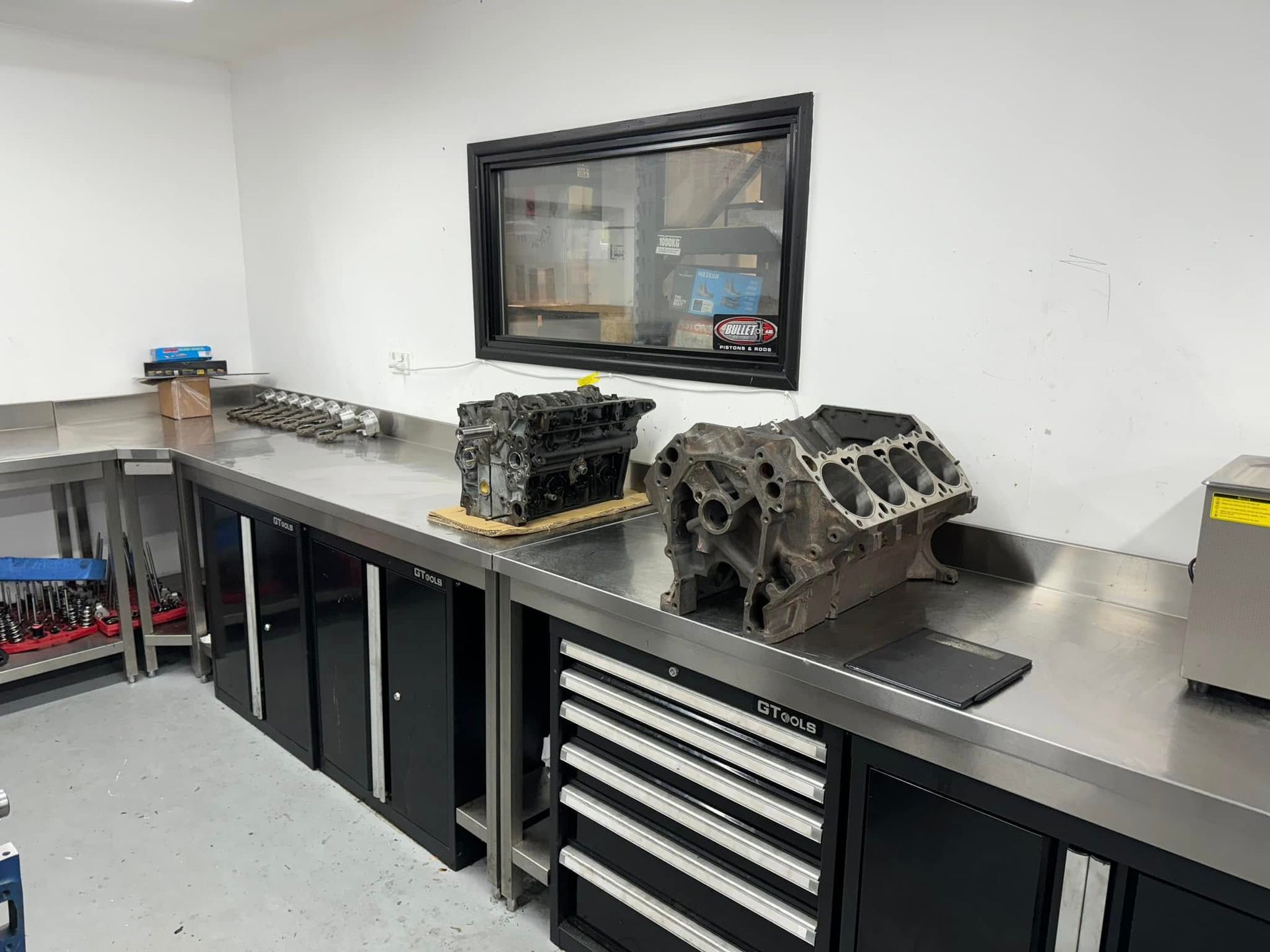 A large engine block is sitting on top of a stainless steel workbench in a garage.