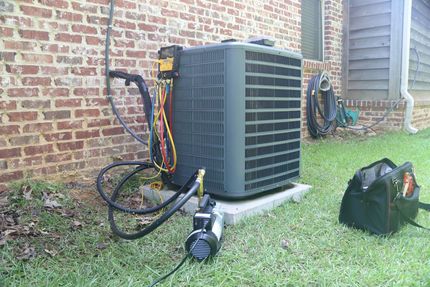 HVAC unit being serviced outside a brick building, with gauges, hoses, and a toolbox on the grass.