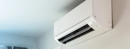 Gray air conditioner unit in a window, supported by metal brackets, on a blue house.