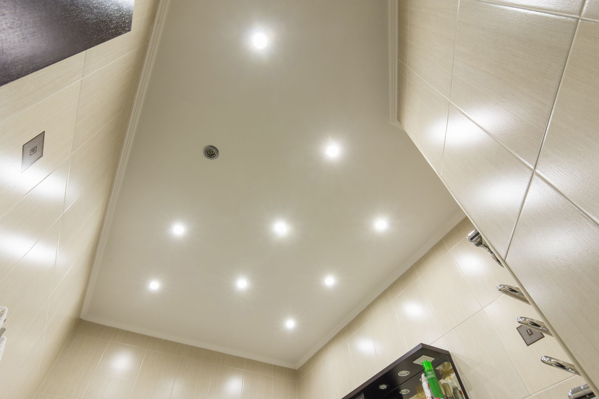 Modern bathroom ceiling with recessed LED lights, beige tiles, and shelf unit for interior design. 
