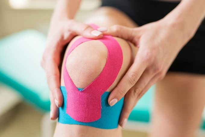 Una donna si sta applicando del nastro kinesiologico sul ginocchio.