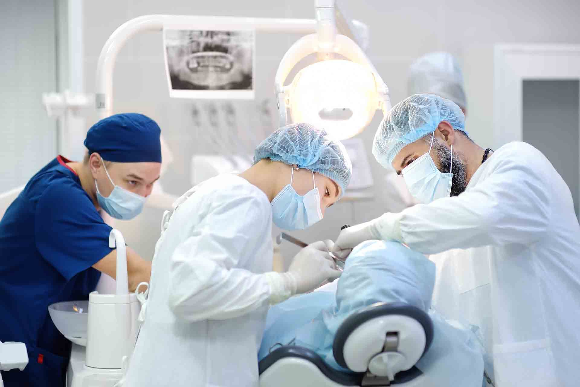 Surgeon and nurse performing dental implant surgery on an anesthetized patient in a modern clinic.