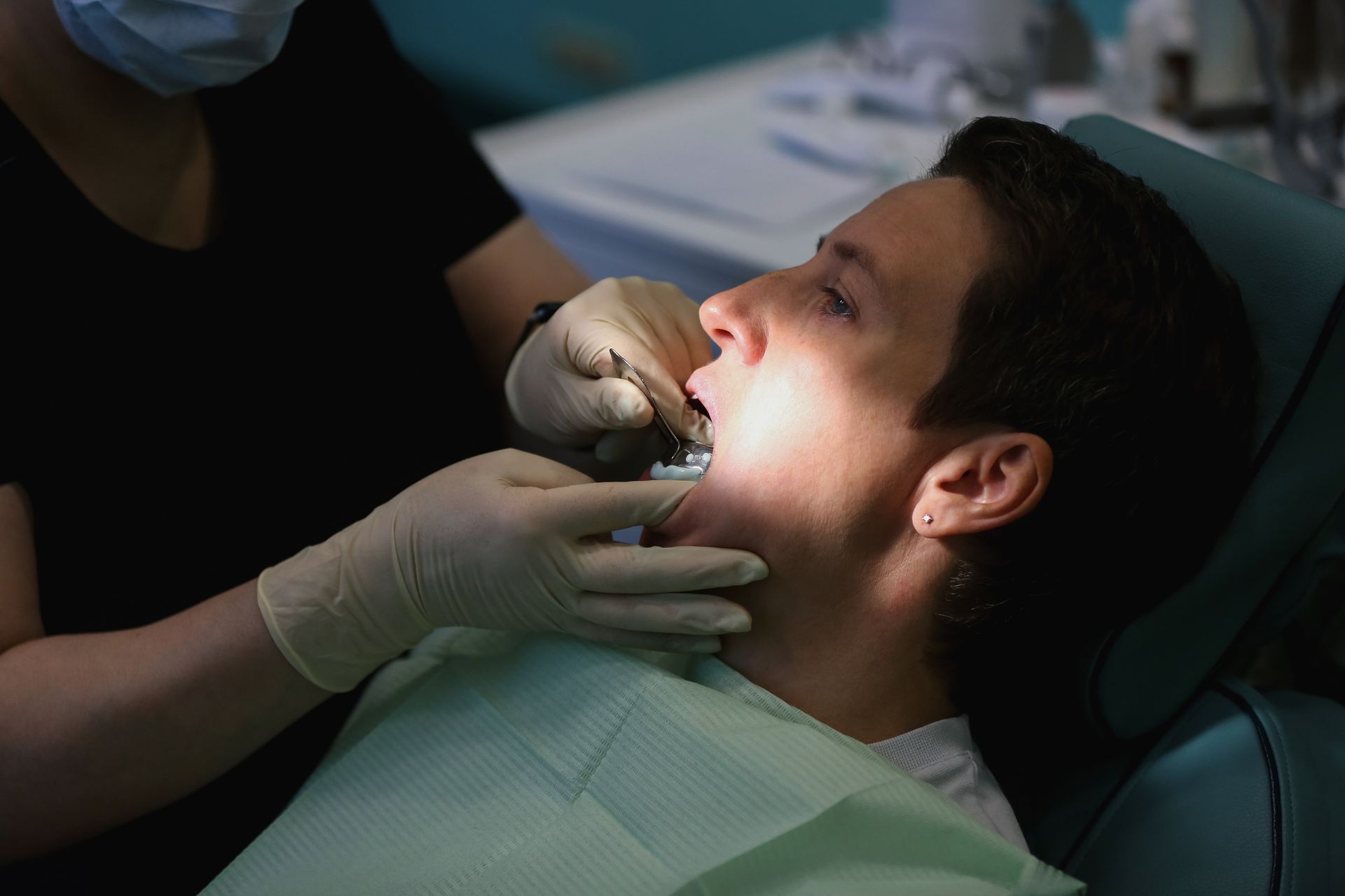 A gloved female dentist examines a patient's teeth during a dental implant prosthesis evaluation. A gloved female dentist examines a patient's teeth during a dental implant prosthesis evaluation.