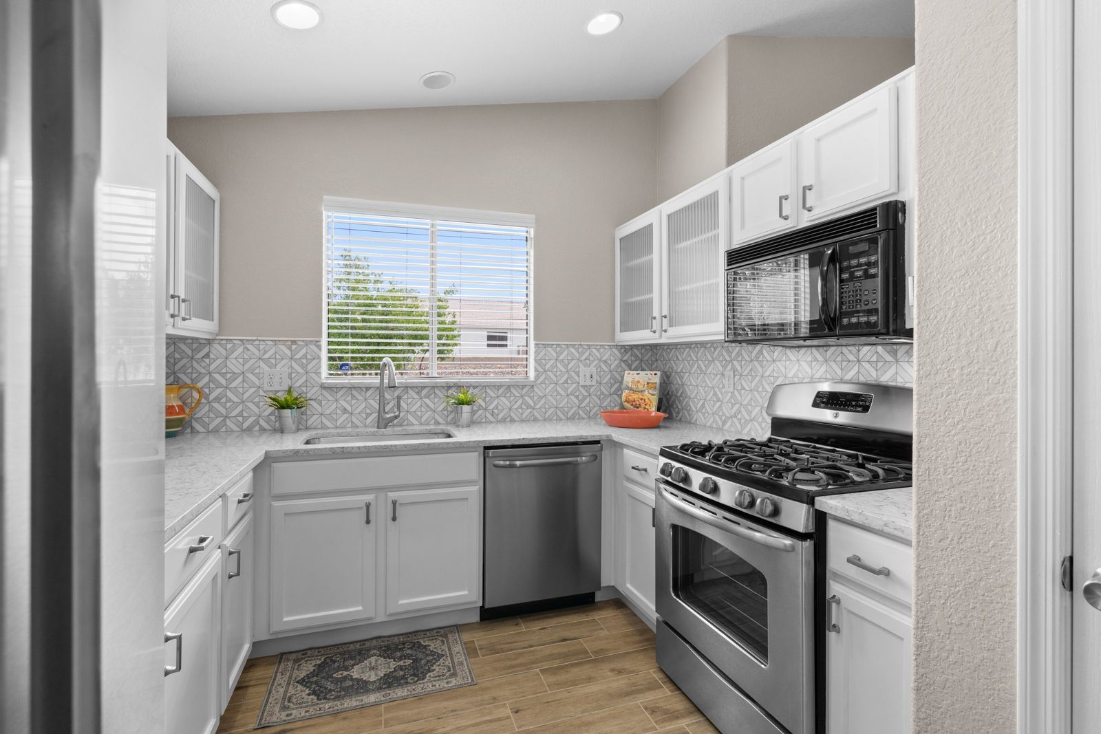 Bright, white kitchen with stainless steel appliances, a window, and patterned backsplash.