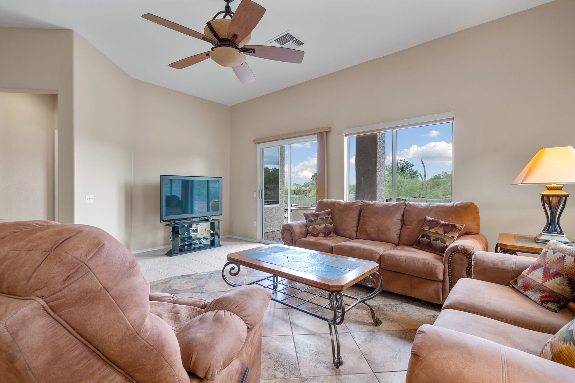 Living room with brown furniture, TV, coffee table, ceiling fan, and large windows.