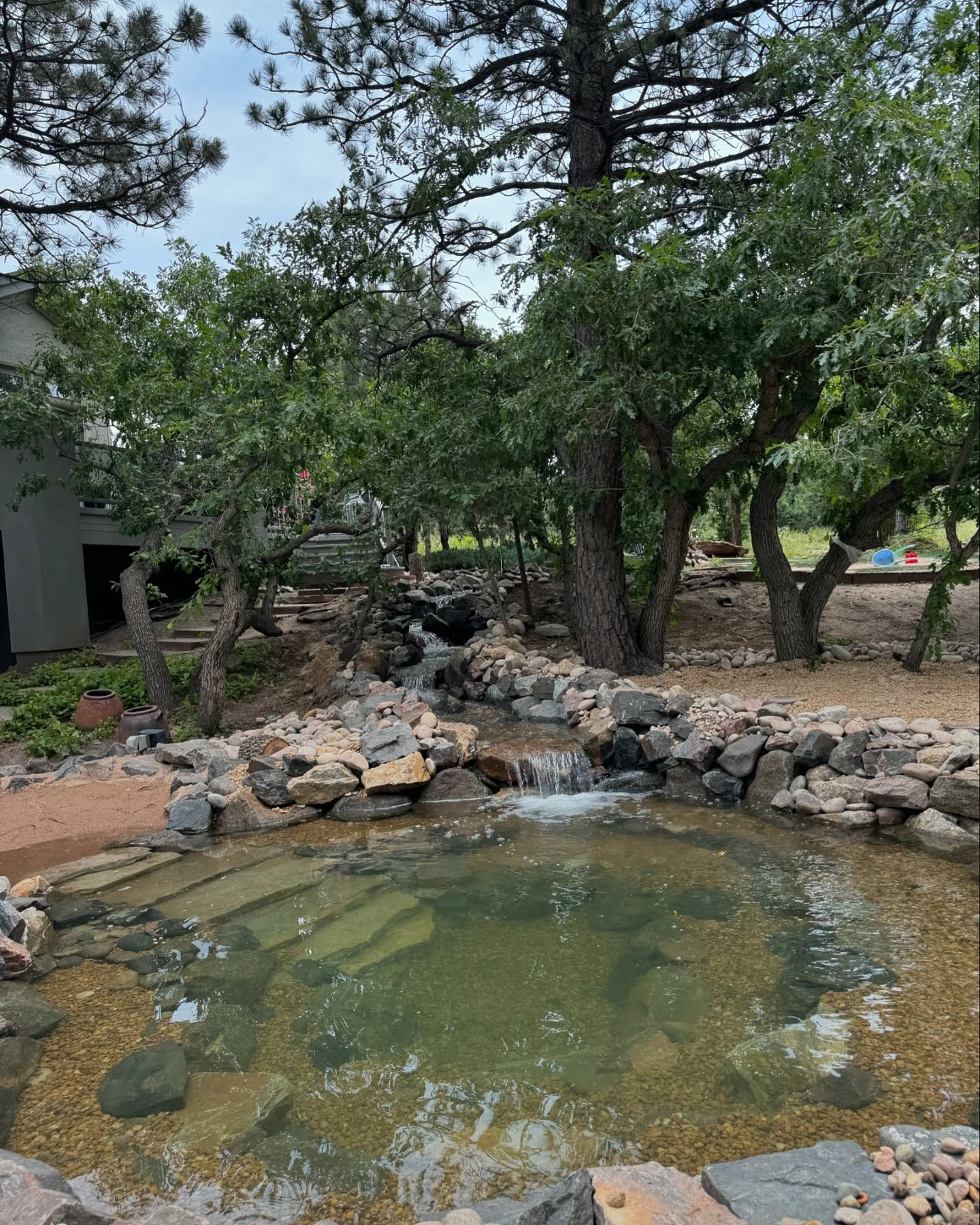 Artificial rock waterfall in a garden, surrounded by plants and trees.